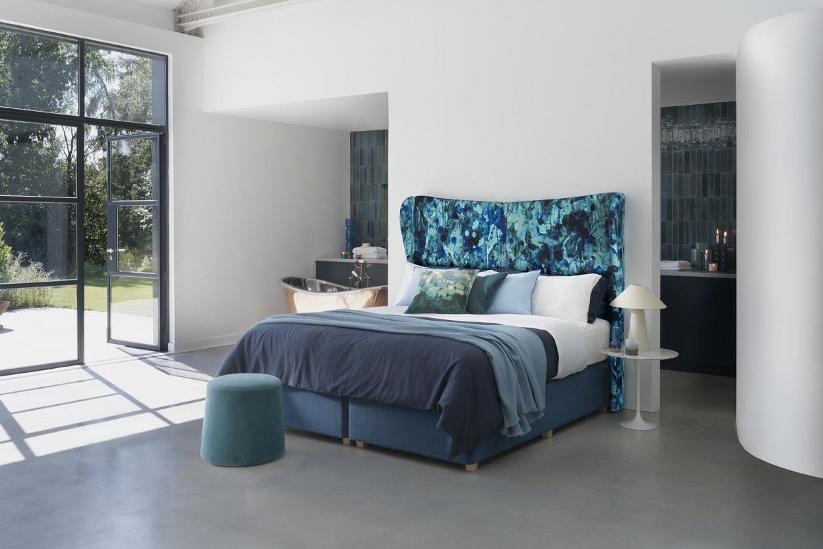 blue hypnos bed in front of glass doors onto a garden
