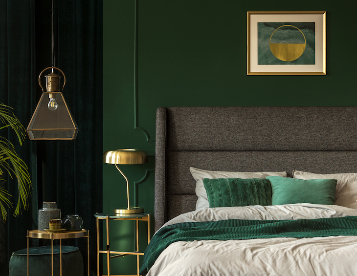 Stylish emerald green and golden poster above comfortable king size bed with headboard and pillows in dark green bedroom