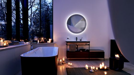A purple lit bathroom with black bath and candles on the floor