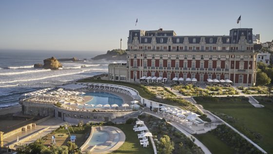 Exterior image of Hôtel du Palais in Biarritz shwing palace like building and crashing waves on the coast