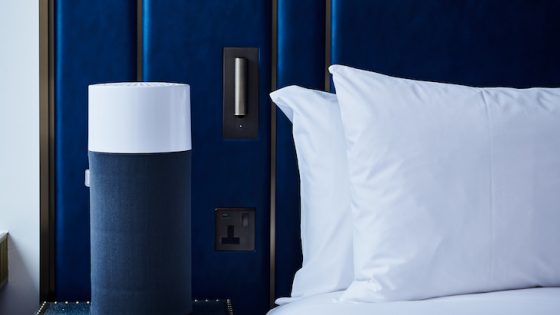 A navy blue air purifier next to a navy blue bed