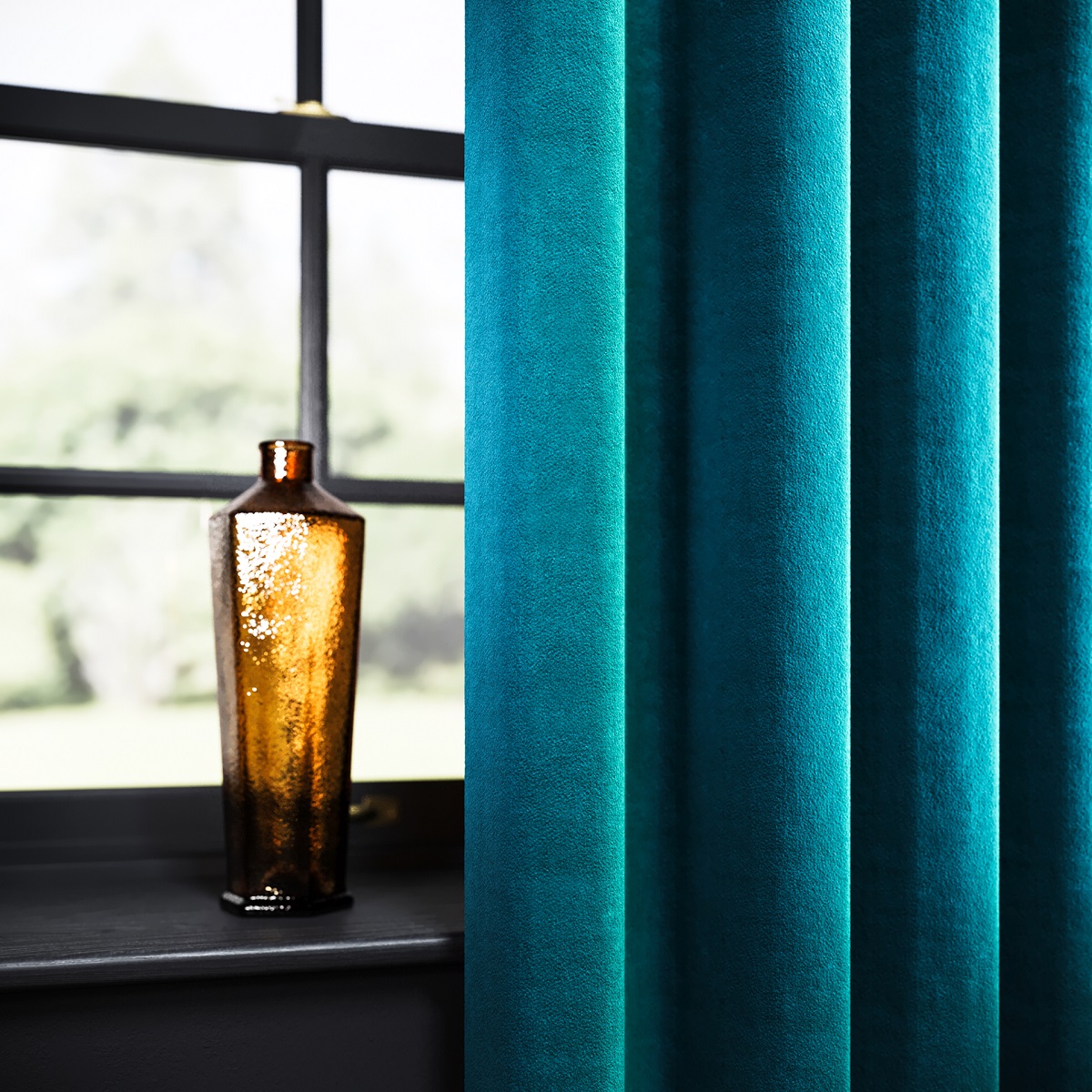 Brookland fabric in teal curtain drape in window setting with amber glass vase