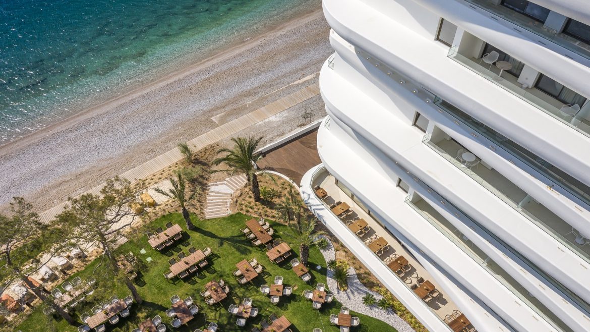 the curved contemporary facade of Isla Brown Corinthia seen from above with a view over the pool and beach