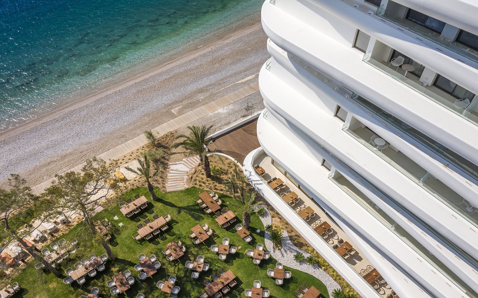 the curved contemporary facade of Isla Brown Corinthia seen from above with a view over the pool and beach