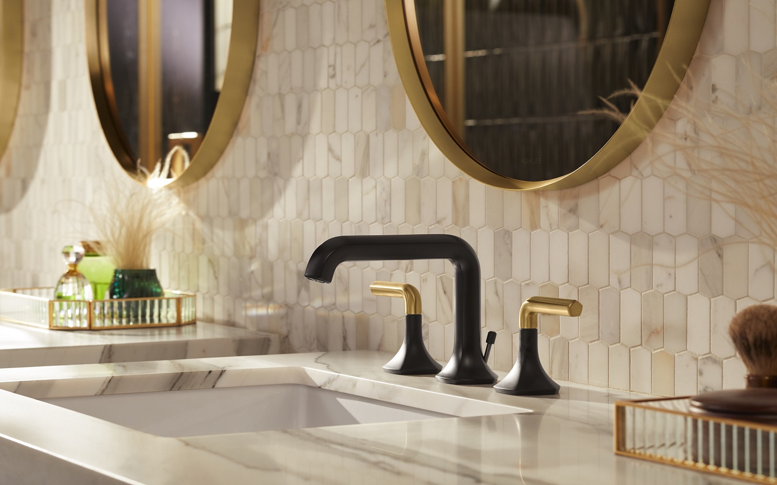 black and gold Kohler taps with marble surface and textured tile wall