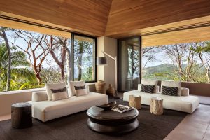 seating area in a villa at Mandarina with white couches, wooden tables and windows looking over the rainforest