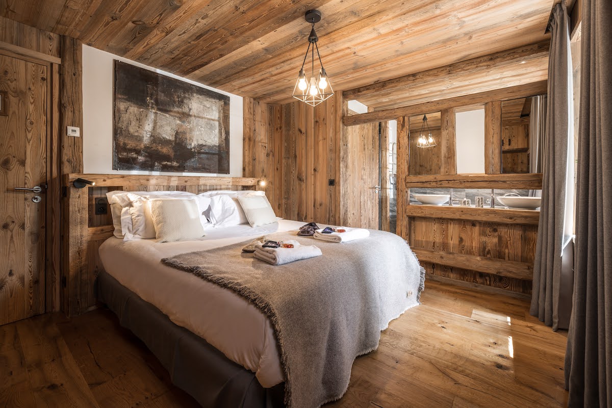 Chalet bedroom with wooden walls and floors and abstract black artpiece above the bed