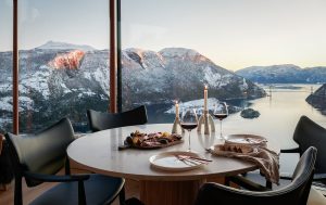chairs and wooden dining table set overlooking the fjords through floor to ceiling glass windows in The bolder