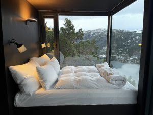 white bed linen in bedroom space in The Bolder surrounded by glass windows looking out over the fjord