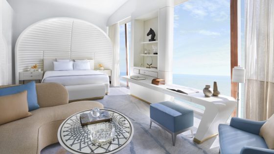 white bed with blue and beige furniture in Fairmonth Doha guestroom suite and living room