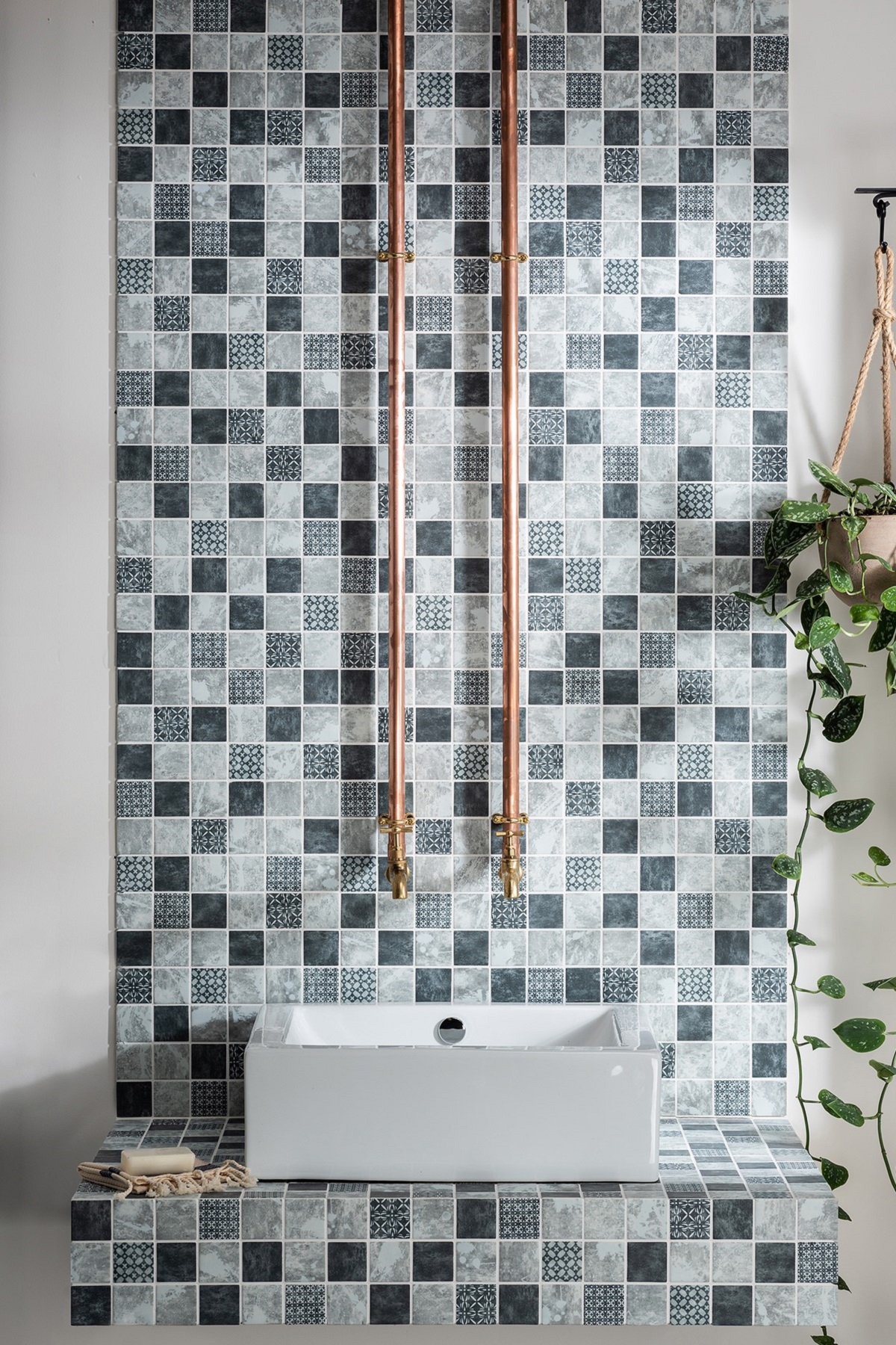 grey square mosaic splashback behind square washbasin and copper pipes with tiles from Hyperion tiles