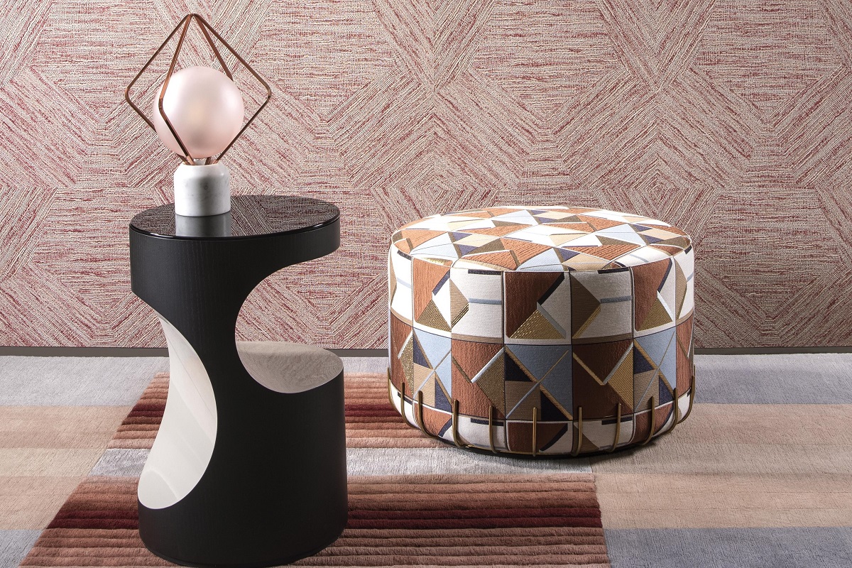 pouffe covered in a geometric print with abstract table and light on a striped carpet and set against arte wallcovering with pentagon abstract design
