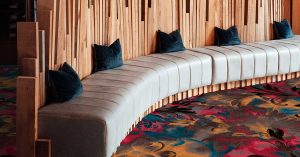 curved wall couch with wood details and blue cushions with Modieus Bello amore carpet in foreground