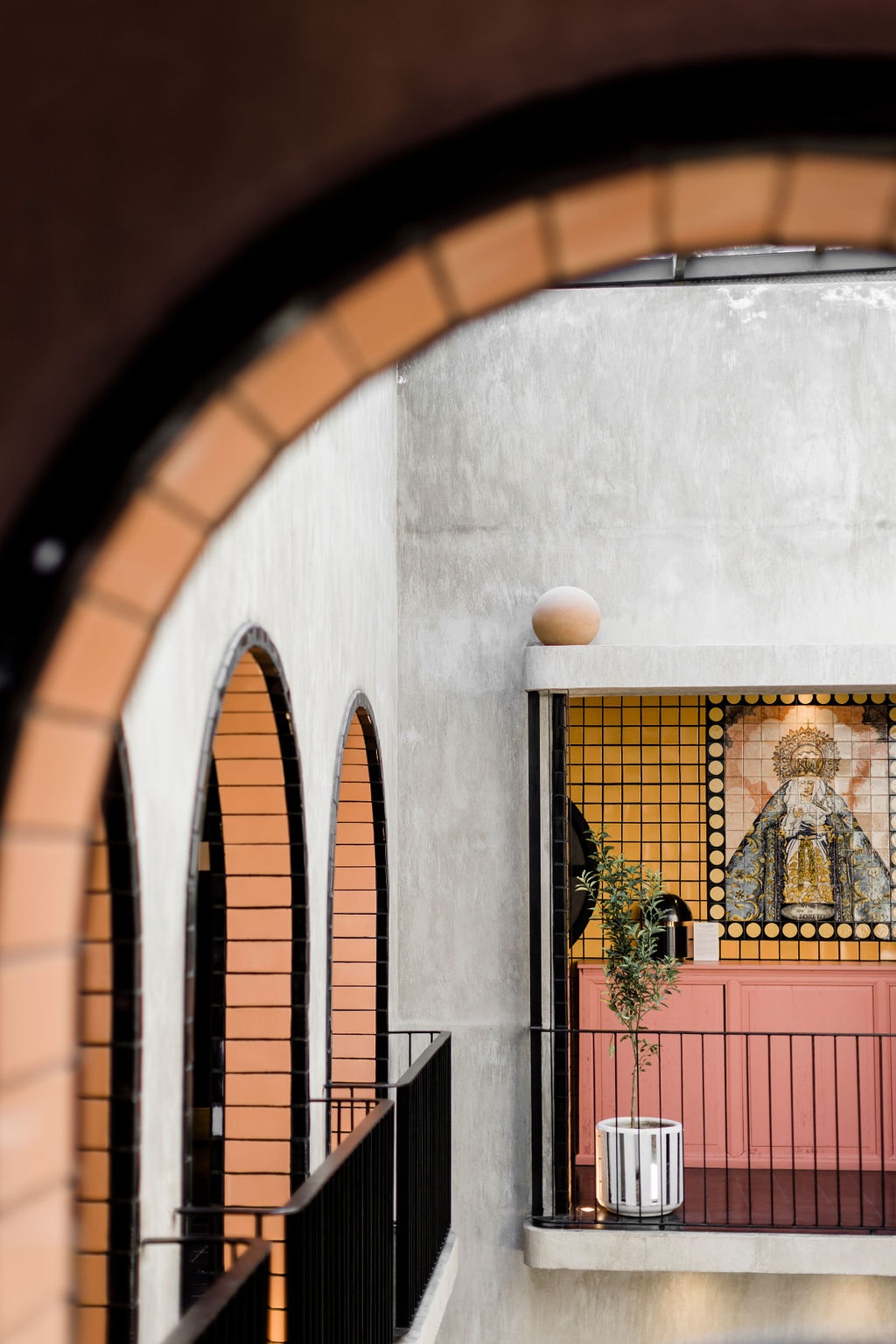 view through arches to pink cabinet, yellow wall tiles and tiled virgin mary on the wall