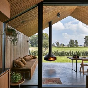 Ergofocus fireplace by FOCUS on the outdoor terrace of a wooden bungalow with views across a field