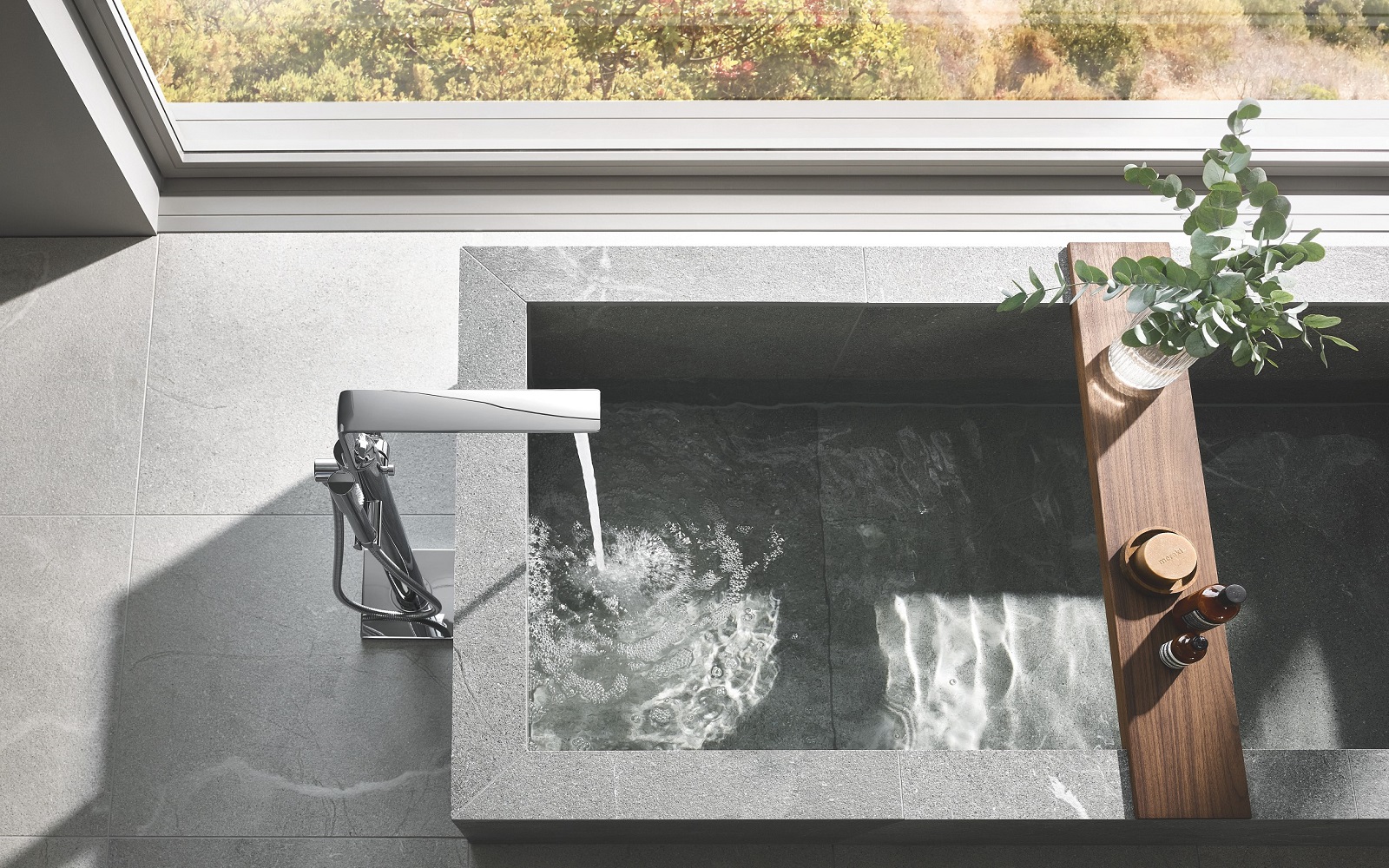 sunken stone bath next to window with water and wood details and mixer from GROHE Allure