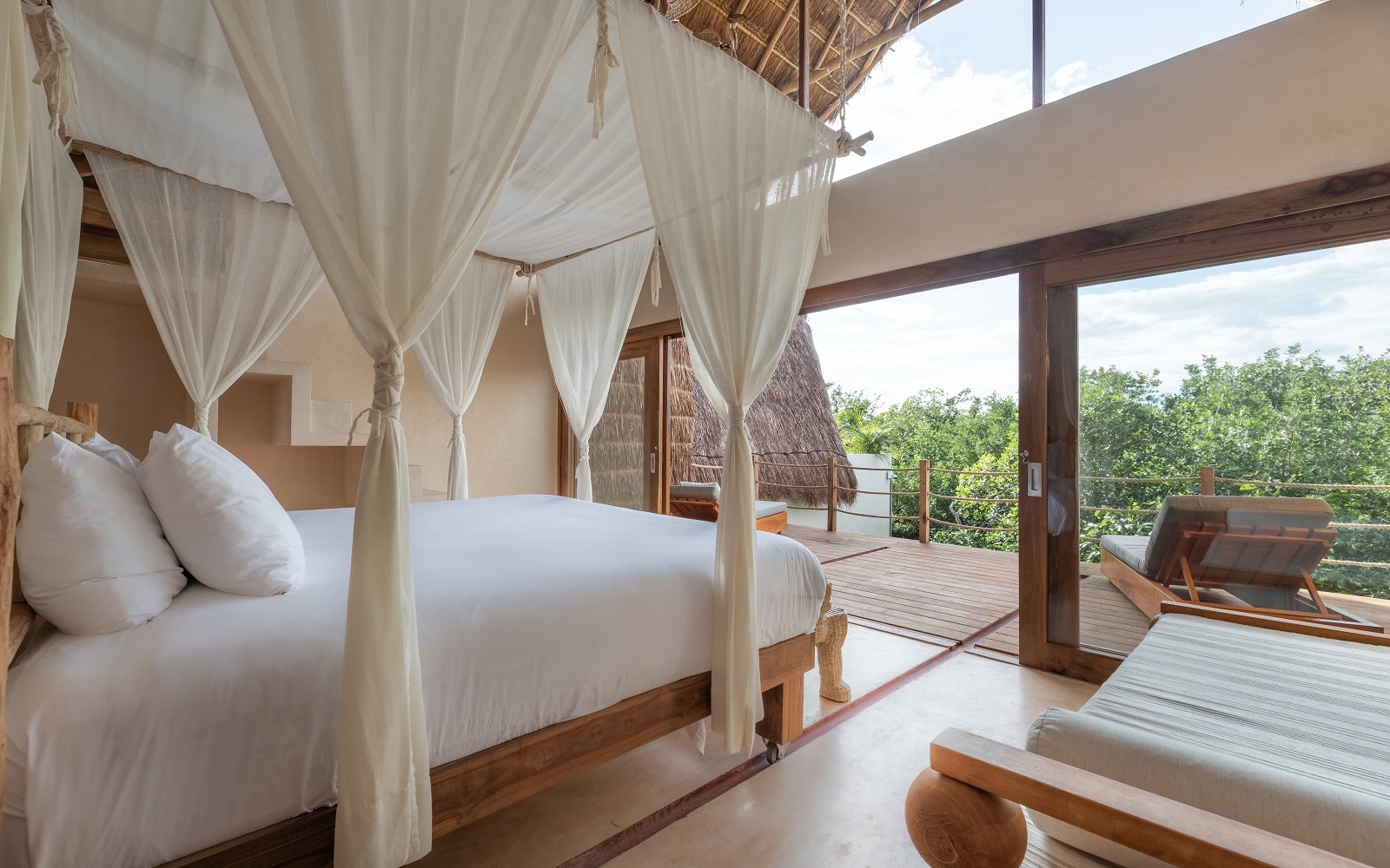 bed draped in fabric with white linen looking out over the Tulum jungle treetops at La Valise