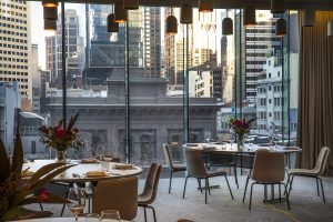 restaurant seating and tables on a grey modieus carpet in voco Melbourne with floor to ceiling windows overlooking the city