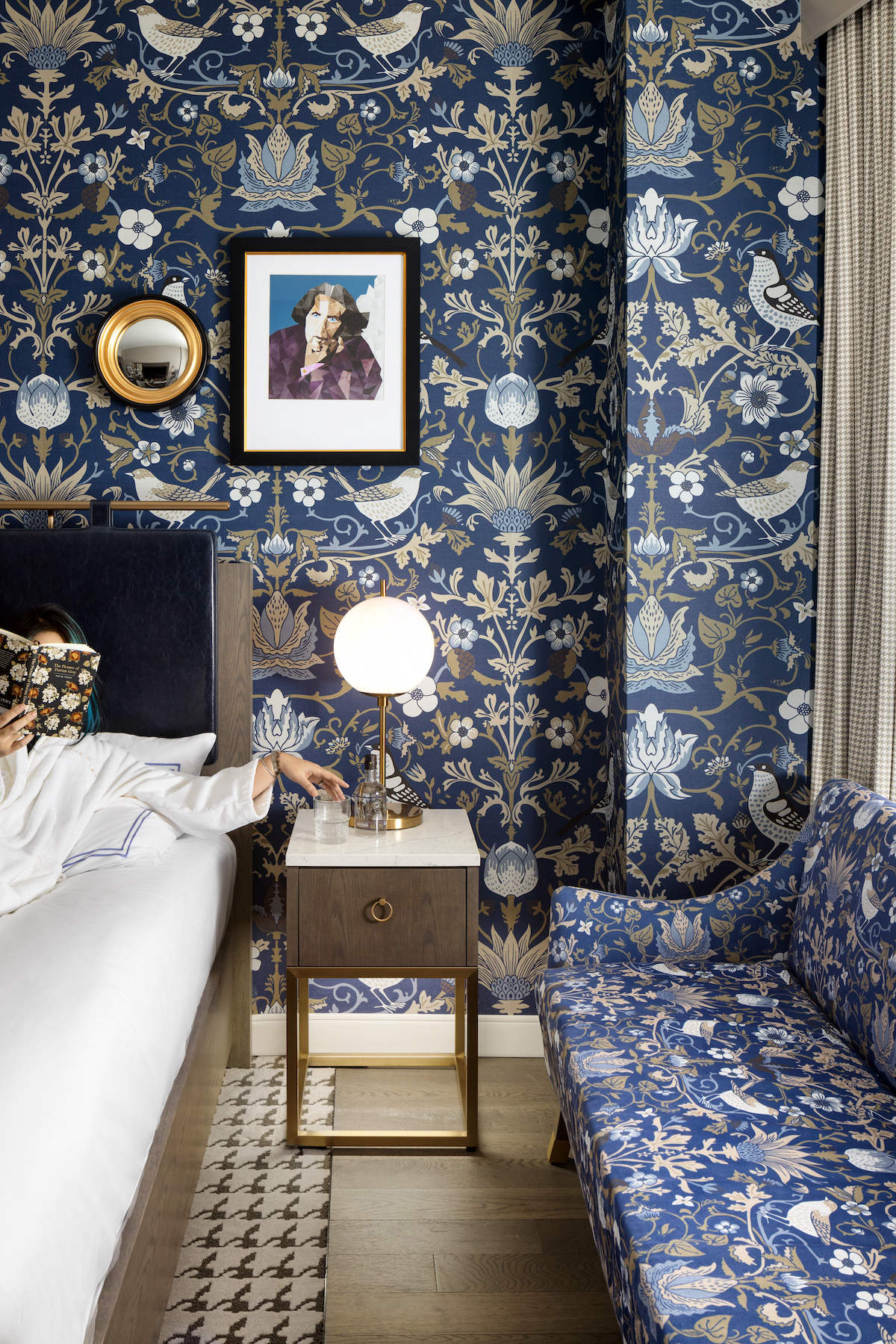 Close up of bedroom in Calgary hotel, with blue patterned wallcovering and woman reaching over to side table