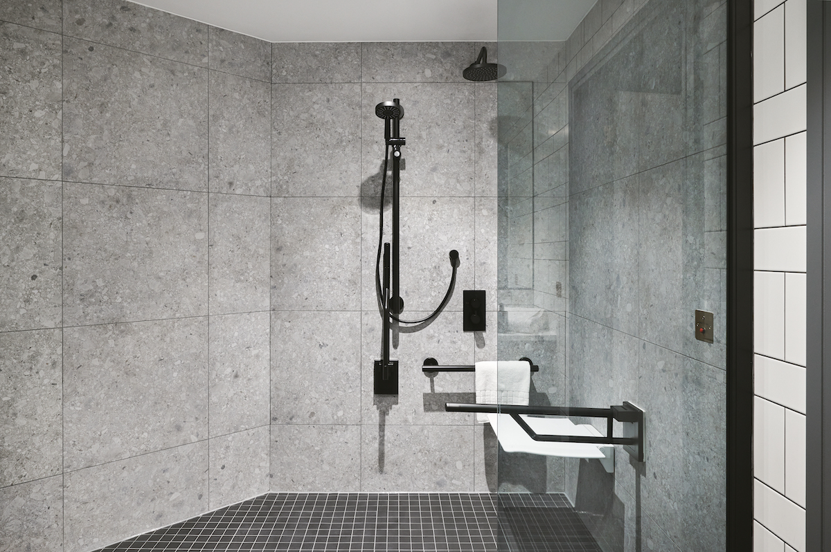 A grey accessible bathroom - large shower unit with black shower and grab rails and bars