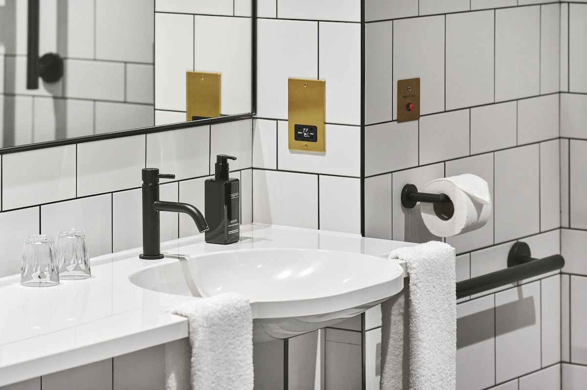 A close-up of a white accessible bathroom showing accents of gold and black
