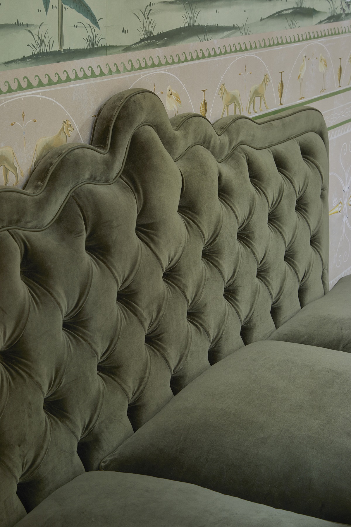 olive green padded and buttoned headboard against vintage patterned wallpaper