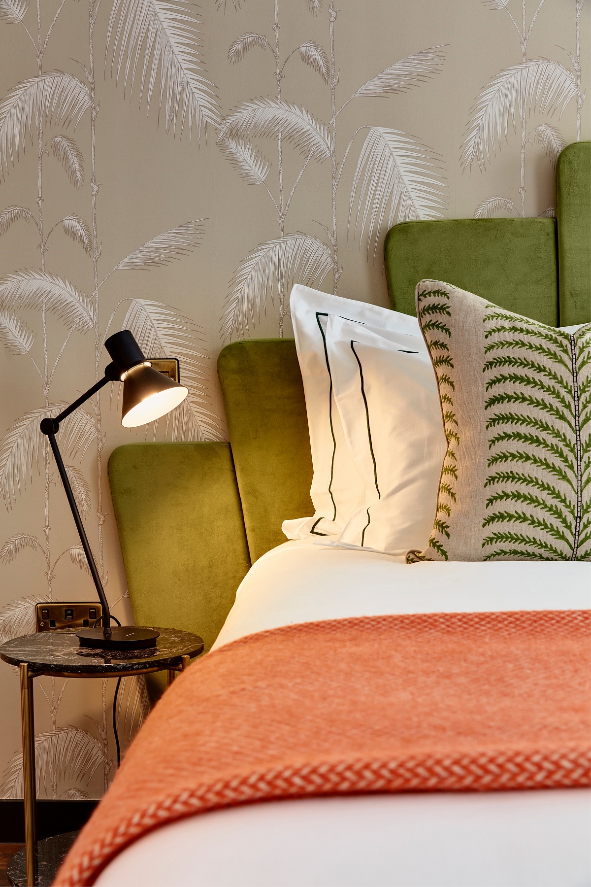 detail of green art deco shaped headboard, oatterend pillow and orange woven throw in guestroom at Brama