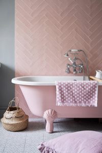 pink herringbone laid tile design behind a pink bath with a white wooden floor