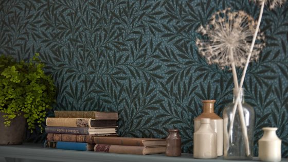 bookshelf with Morris & Co willow wallpaper in green behind books and vases