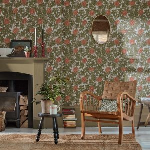 rambling rose wallpaper in green and pink on wall in cottage with fireplace and a wooden chair