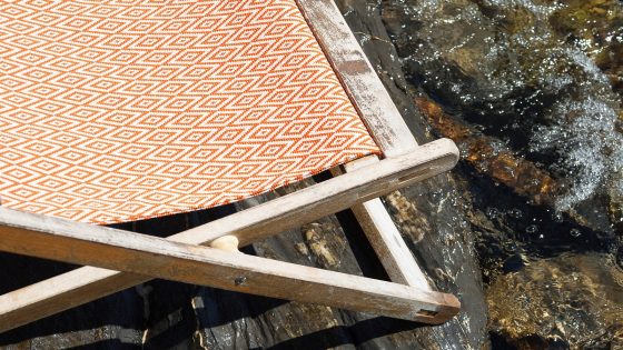 deckchair covered in Dedar fabric sitting on rocks on the edge of the water