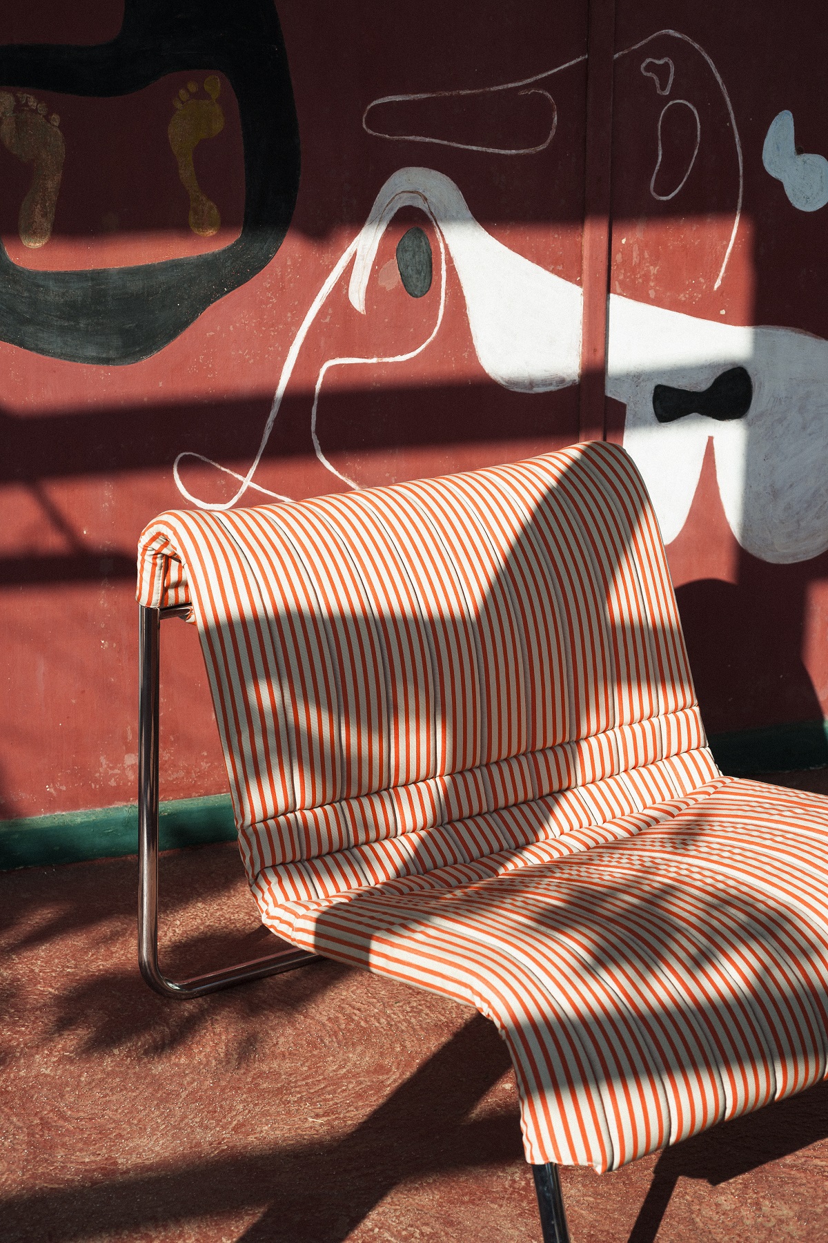 outdoor chair in striped Dedar fabric against a painted mural wall in rust