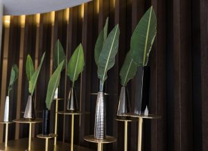 silver vases on plinths in a row with single leaves on display in Westin against wood panel wall