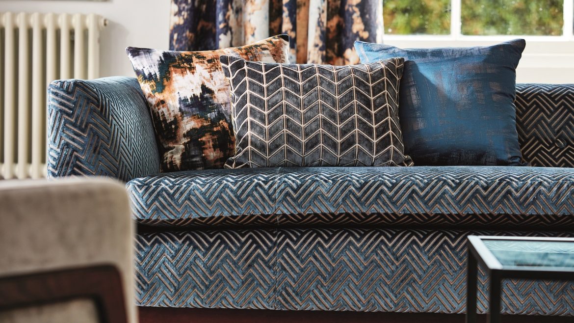 blue upholstered sofa with cushions in different patterns in front of a window - fabric by Harlequin