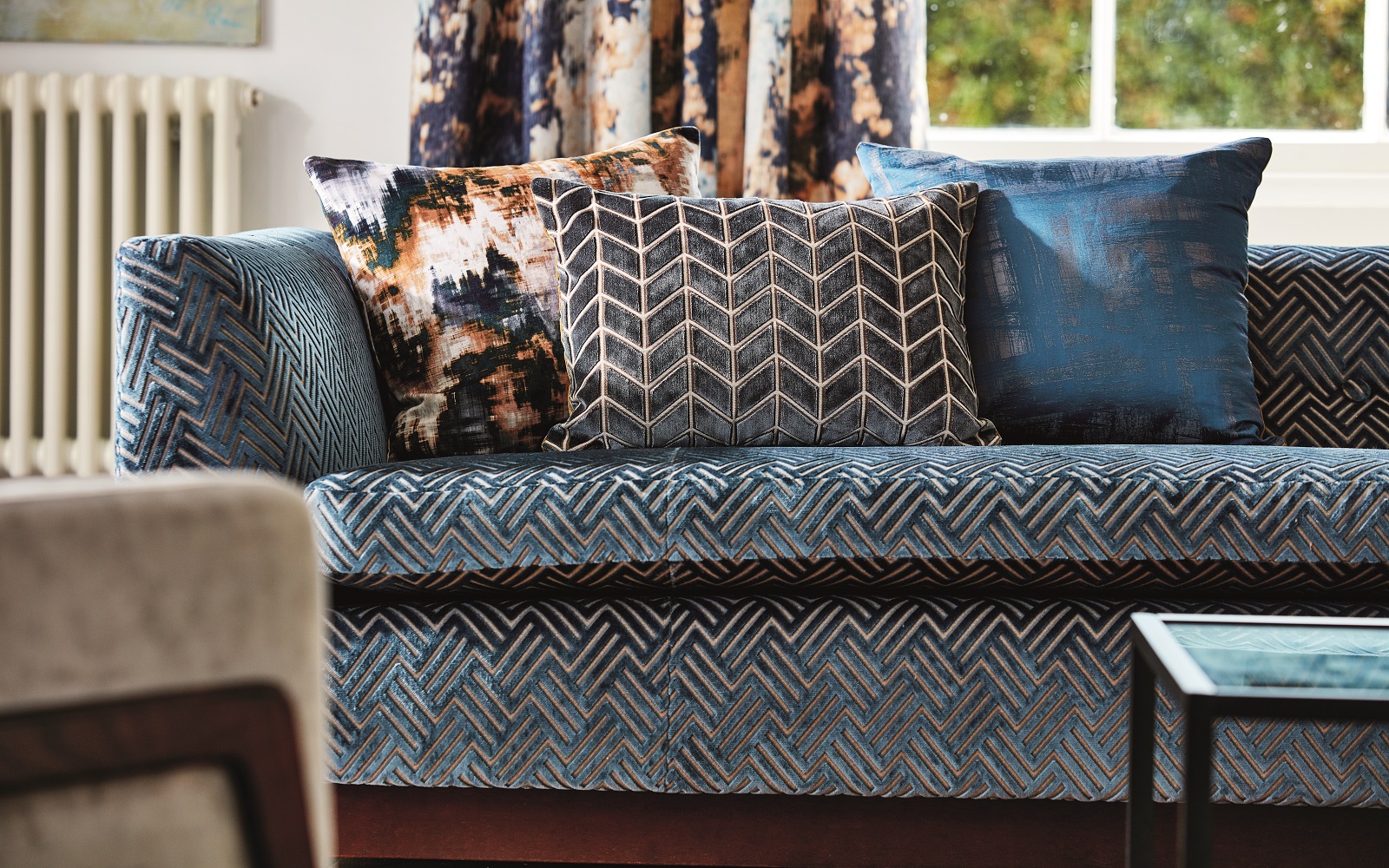 blue upholstered sofa with cushions in different patterns in front of a window - fabric by Harlequin