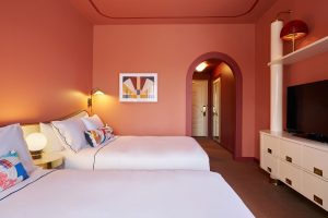terracotta painted walls and ceiling with two double beds and patterned cushions in guestroom