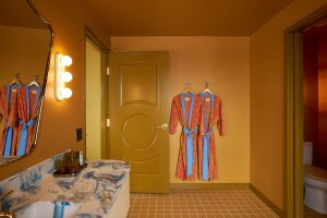 bathroom in Hotel Genevieve with yellow walls and ceiling, curved marble console and kimonos