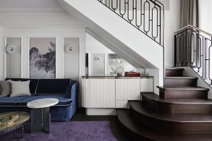 stylised floral pattern cut into the purple carpet with dark blue sofa and wooden staircase