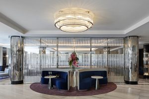 art deco inspired entrance and lobby to The royce Hotel with silver pillars and blue seating under a central chandelier