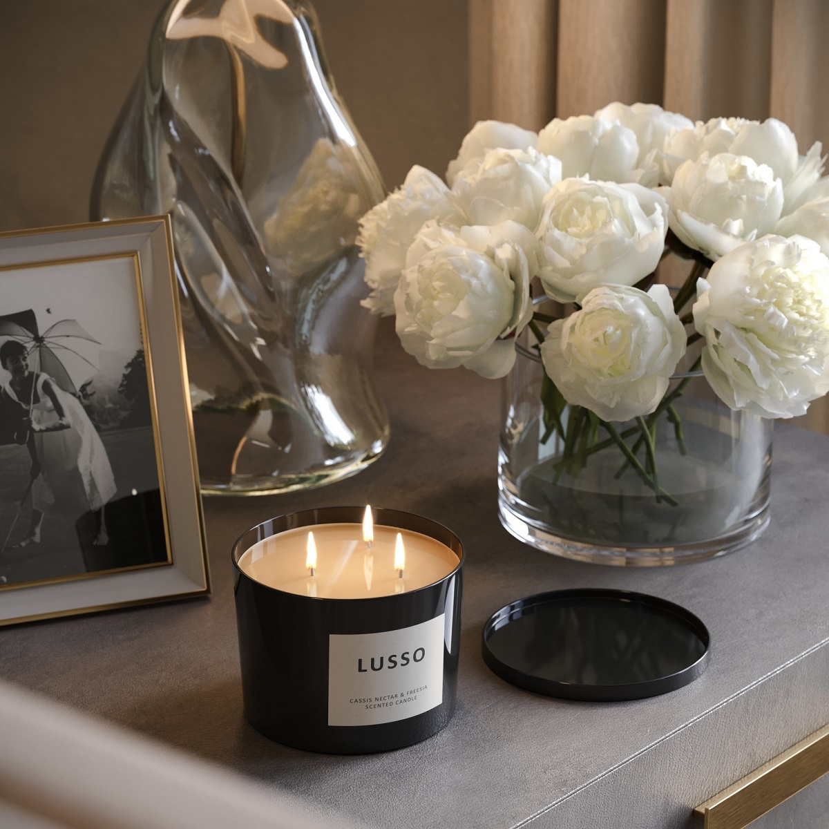 scented three wick candle glowing on a sidetable with flowers and picture frame