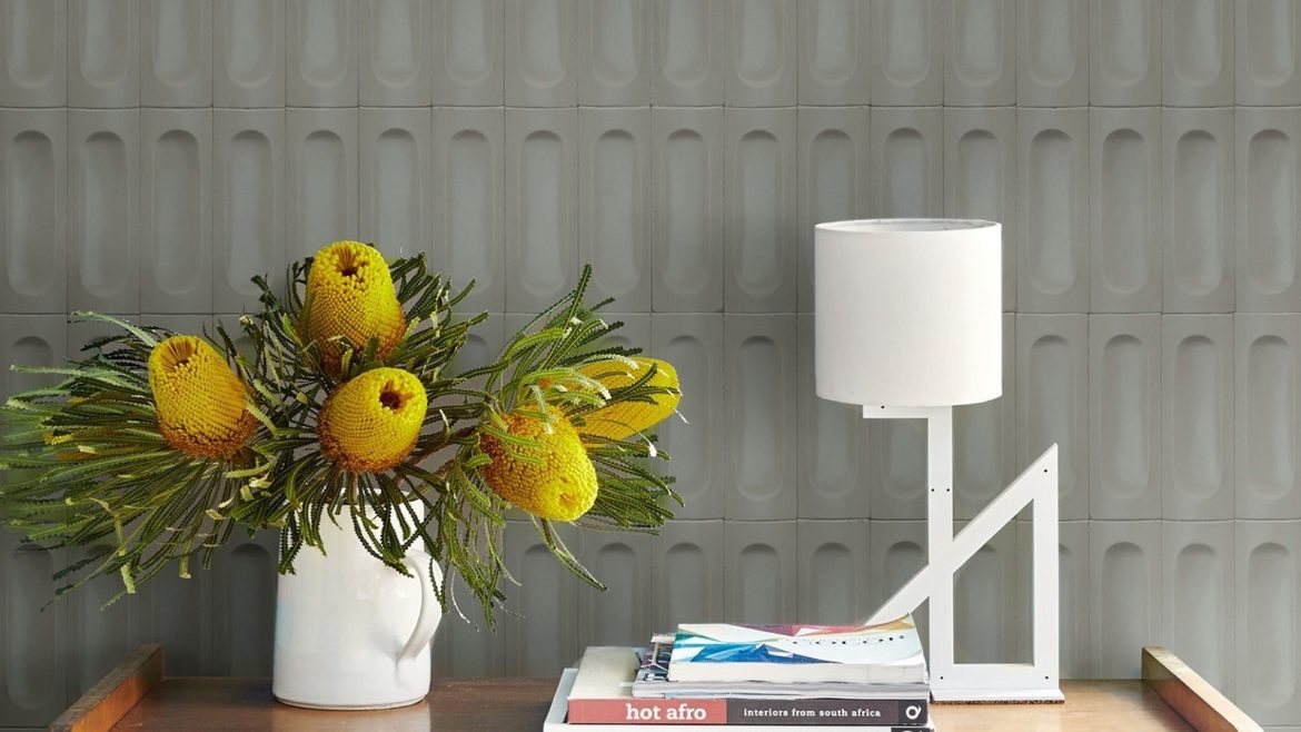 yellow proteas in a white vase with books and white lamp on wooden table in front of grey Parkside wall tiles