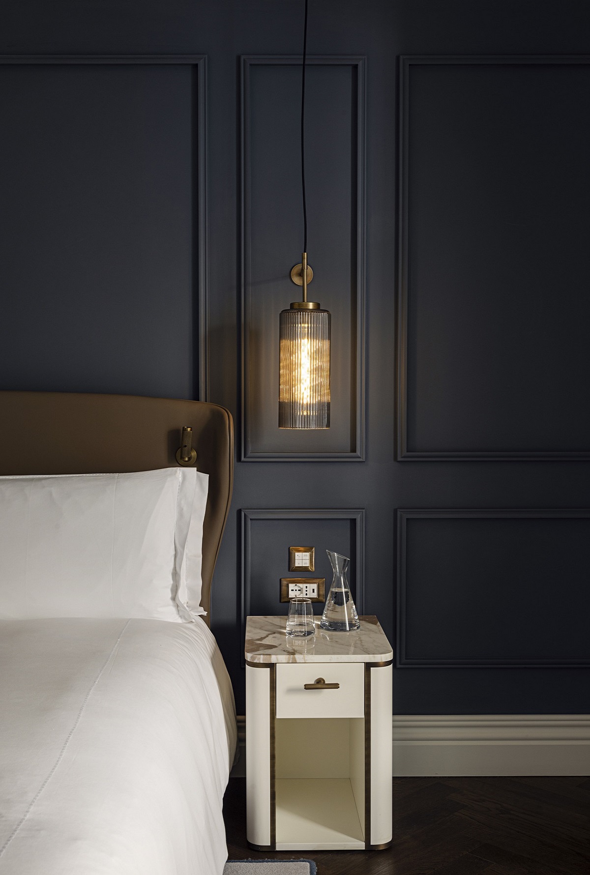 dark painted panelled wall behind bed with white linen and suspended bedside light