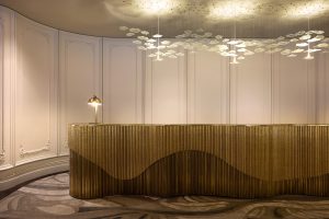 curved reception desk with statement chandelier above and patterned carpet below all in neutral colours in the Playford Hotel Adelaide