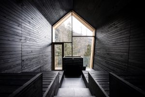 black wood interior of sauna with end wall in glass and views onto the dolomite mountains