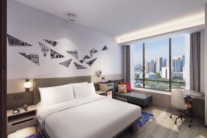 guestroom with white bed and wooden floor and geometric shard design on the wall with views over Singapore in Aloft Singapore