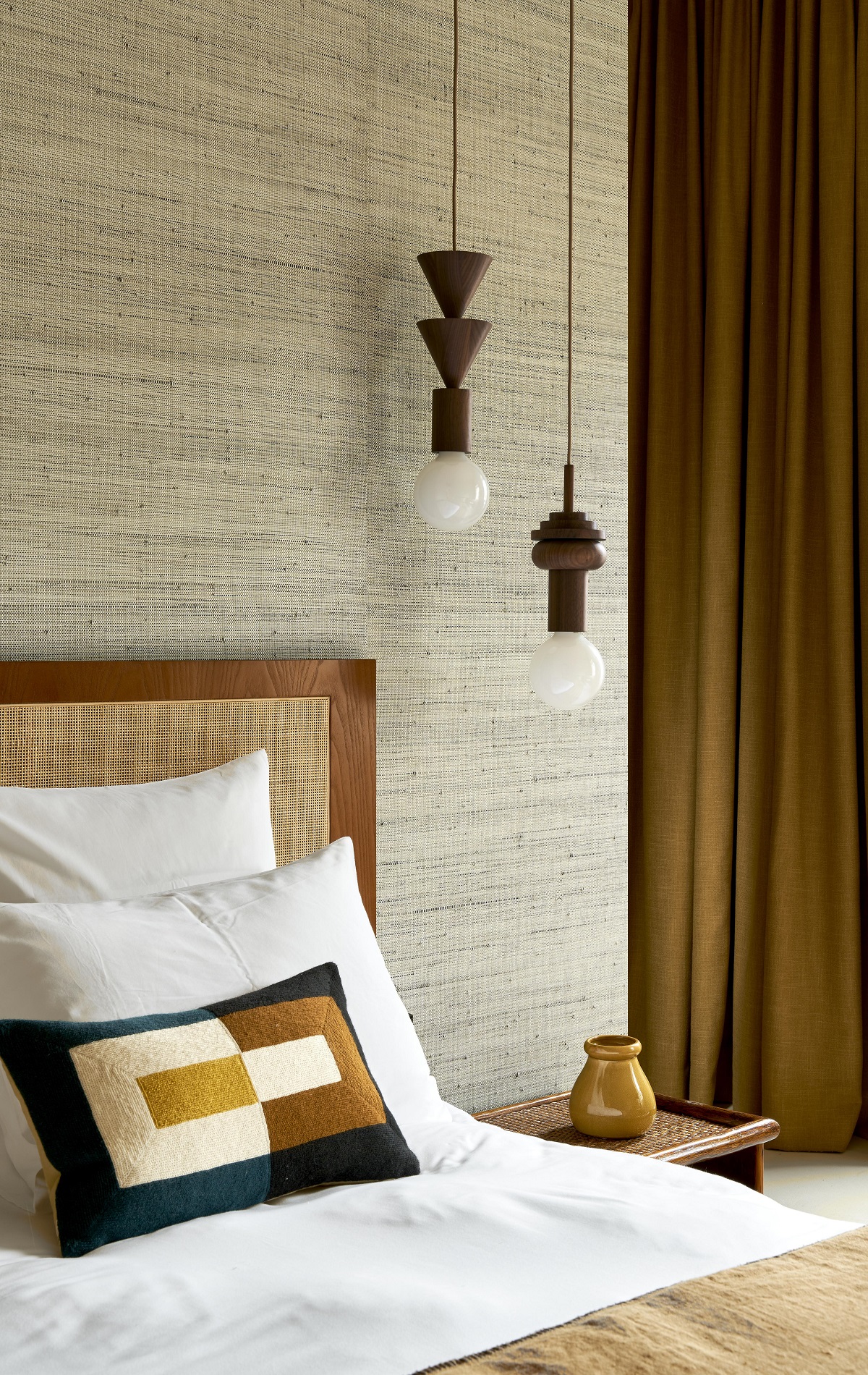 textured natural wallcovering behind bed with graphic patterned cushion and wooden light detail