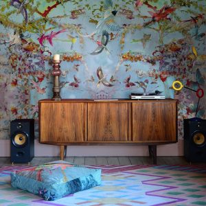 Maximalist floral wallpaper behind a mid-century wooden cabinet and a chevron pattern colourful rug in room designed by Blackpop