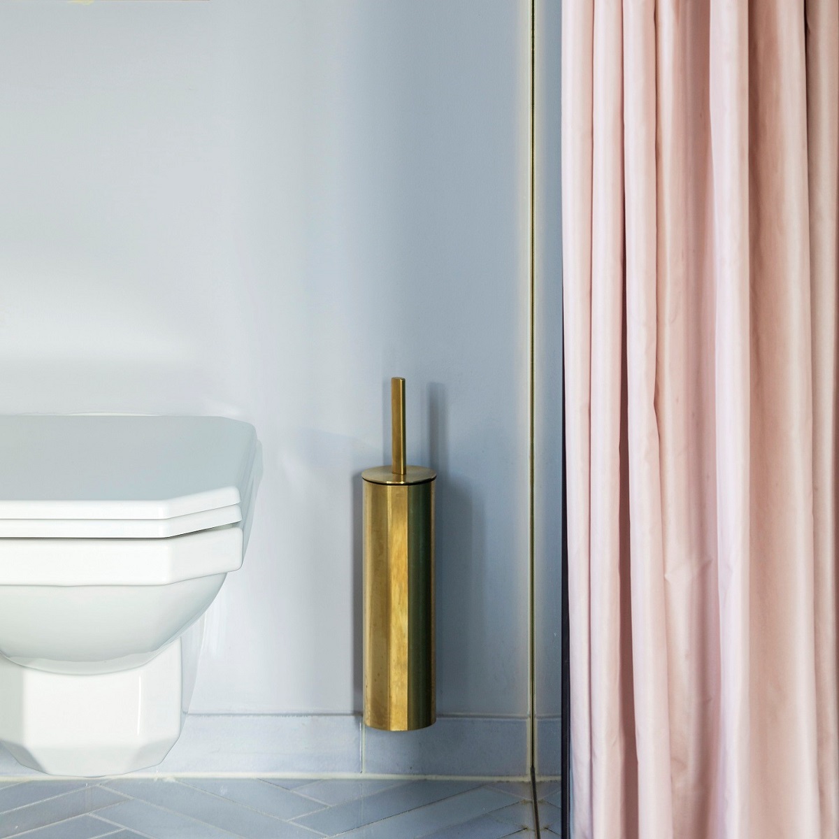 white vintage style toilet against blue wall with pink shower curtain and brass fitting details