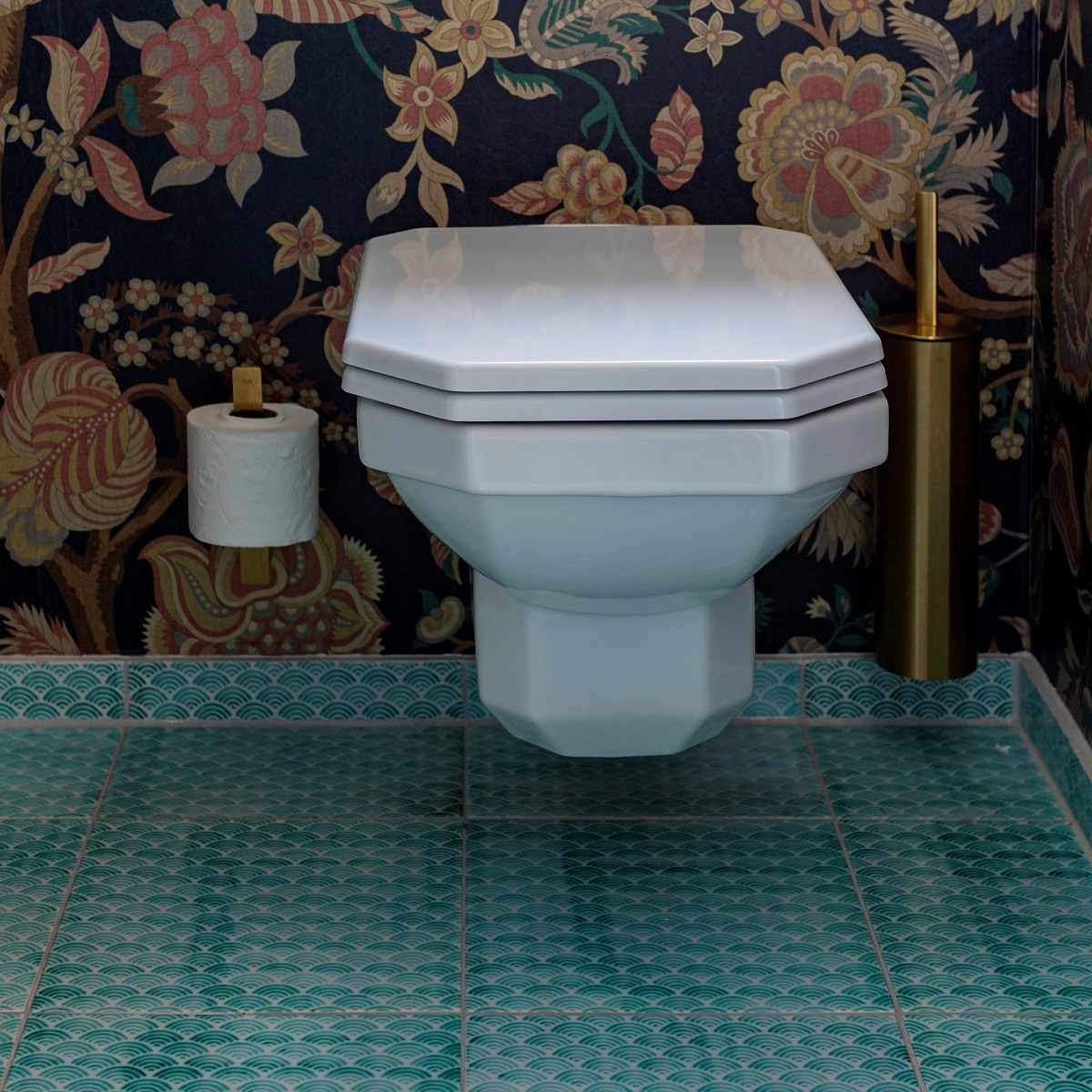 vintage style wall hung toilet against floral wallpaper and with brass unidrain fittings