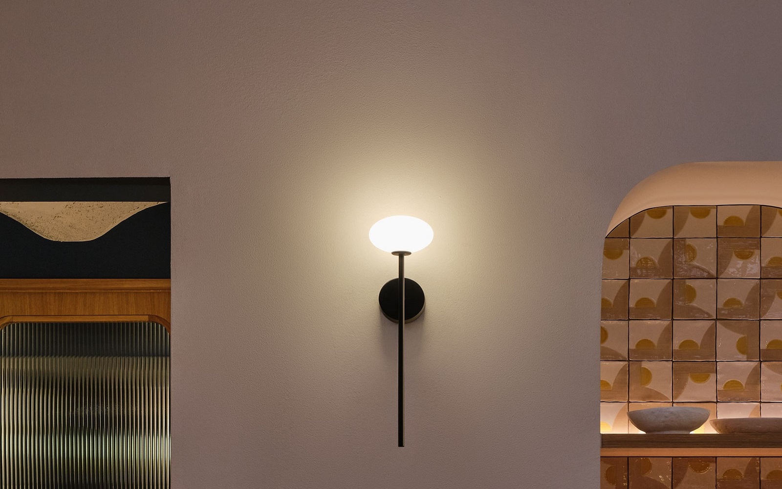 single black Bloom wall light by LEDSC4 on cream wall with patterend tiles in background